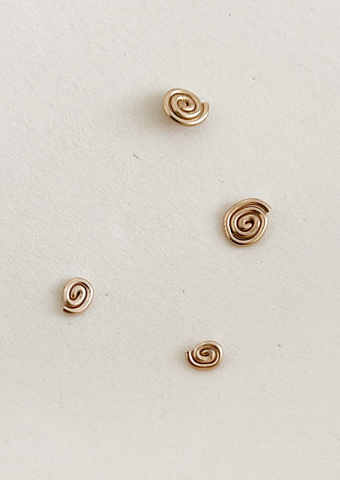 Four gold spiral earrings on a light gray background